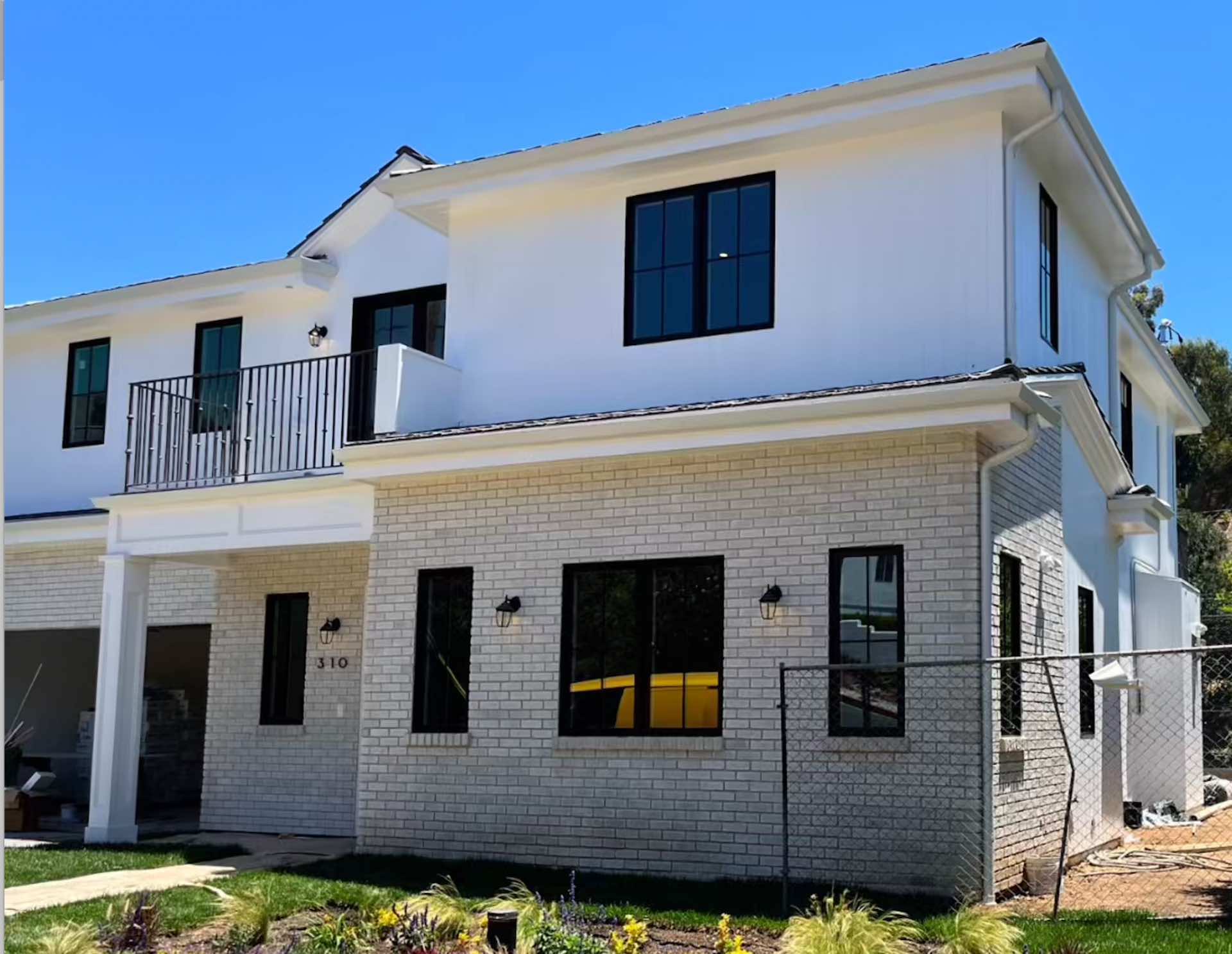 Two-story room addition with white stucco exterior, painted brick accent, black window frames, and covered balcony - New Dawn Construction